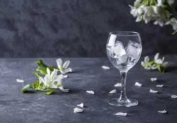 Empty wine glass with ice cubes on a dark background, with apple tree flowers. Copy space for text, low key