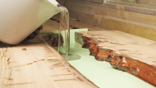 Carpenter pouring epoxy resin over wooden table. Furniture manufacture