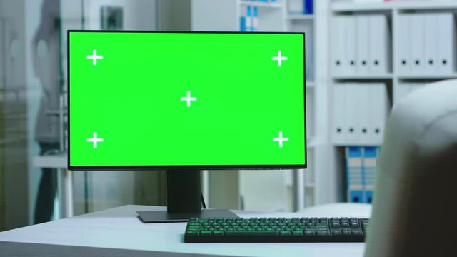 Dolly shot of computer with green screen in private hospital and personnel wearing uniform in the background. PC with blank and copy space green screen available on display of medicine specialist in
