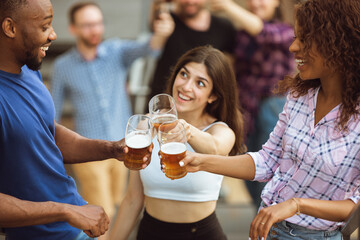 Group of happy friends having beer party in summer day. Resting together outdoor, celebrating and relaxing, laughting. Summer lifestyle, friendship concept. Clinking beer's glasses, cheerful, happy.