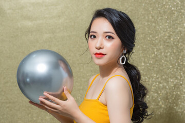 Naklejka premium Beautiful young Asian woman holding ballon when standing isolated over gold background.