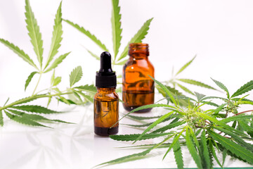 Bottle with cannabis oil against hemp leaves on a white background.