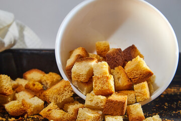 Square toasted pieces of homemade delicious rusk, hardtack, Dryasdust, zwieback on a white plate and baking sheet.