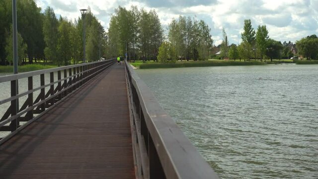 Unrecognizable woman walking with bicycle on long wooden bridge over lake