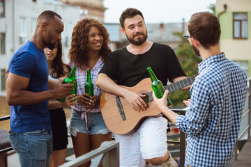 Group of happy friends having beer party in summer day. Resting together outdoor, celebrating and relaxing, laughting. Summer lifestyle, friendship concept. Playing guitar, singing, cheerful.