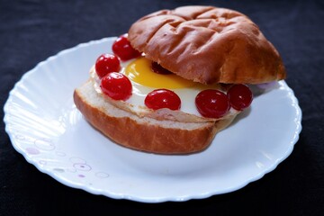 Homemade burger bun with fried egg and red cherries on a white plate . Top view image.