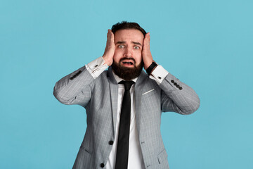 Frightened corporate employee grasping his head in terror over blue background