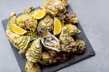 Fresh opened Oysters close-up on black plate with sliced lemon and ice. Healthy sea food. Gourmet food. Flat lay, top view, mockup, overhead, template with copy space. Online order and food delivery