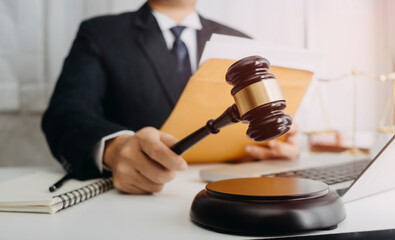 Justice and law concept.Male judge in a courtroom with the gavel, working with, computer and docking keyboard, eyeglasses, on table in morning light