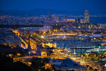 Fototapeta premium Aerial view of Barcelona city skyline with city traffic and port with yachts illuminated in the night. Barcelona, Spain