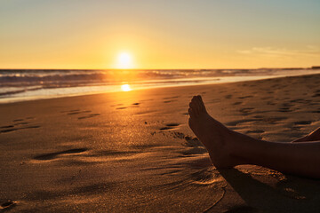 Women's legs on the beach at sunset. Concept of beach, vacation and travel.
