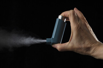 Close up view of blue asthma inhaler with spray coming out. Black background