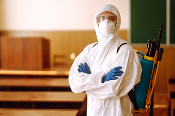 Fototapeta na wymiar Portrait of man in protective hazmat suit with spray chemicals disinfecting school class. COVID-19.
