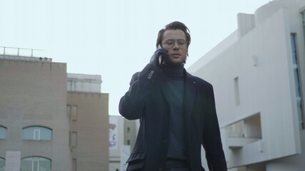 Smiling businessman calling on phone at street. Happy executive walking outdoors