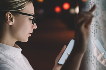 Digital monitor with public transport subway map. Female standing at big display with smartphone in hand. Young woman touching with finger screen while using train schedule application on mobile phone