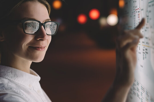 Female in glasses standing at display with advanced innovative technology. Young woman touching with finger screen while selecting surface option. Interactive kiosk with night light reflected on face