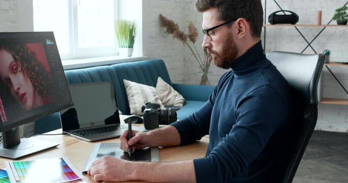 Professional Stylish Photographer in eyeglasses Works in Photo Editing App or Software on His Personal Computer. Photo Editor Retouching Photos of Beautiful Girl in Home-Office. Freelance Profession.