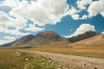 Dirt road in mountains. White clouds blue sky of Central Asia, at the height of 4,000 meters