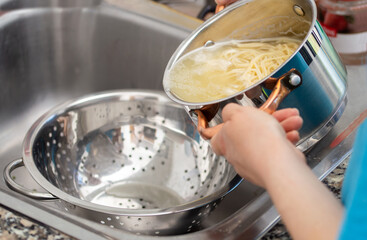 woman separating water from spaghetti withempty silver colander - obrazy, fototapety, plakaty