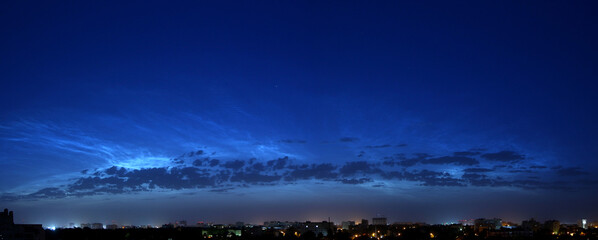 Panorama of a beautiful blue predawn sky with silvery mesospheric clouds. Noctilucent clouds. Late twilight. Night city. The sun is beyond the horizon.