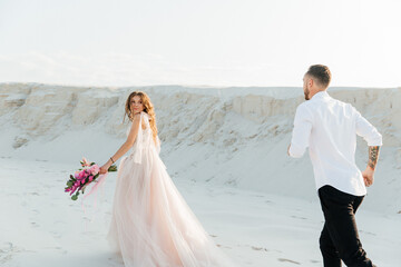 Fototapeta na wymiar Love Story of a beautiful couple in a pink wedding luxury dress with a bouquet in the Sahara desert, sand, dunes
