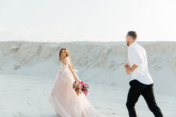 Fototapeta na wymiar Love Story of a beautiful couple in a pink wedding luxury dress with a bouquet in the Sahara desert, sand, dunes