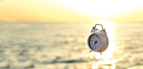 white alarm clock soars in the air on the beach against the background of the sea and dawn. The concept of a good morning and a wonderful day. Morning on the beach at sunrise.