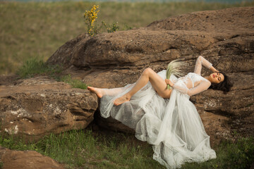 Naklejka premium beautiful young female with makeup and hairstyle in a gentle wedding peignoir lies on the stones outdoors