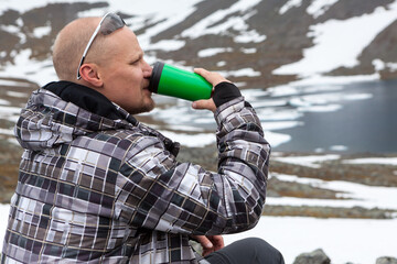 Portrait of Caucasian man drinking energy drink or coffee on the mountain peak, one climber or mountaineer in mountains