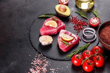 Fresh tuna fillet steaks with spices and herbs on a black background