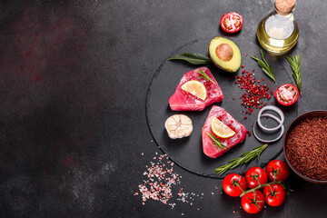 Fresh tuna fillet steaks with spices and herbs on a black background