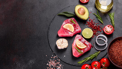 Fresh tuna fillet steaks with spices and herbs on a black background
