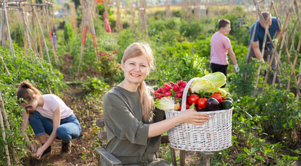 Positive woman posing with basket of ripe vegetables on farm field