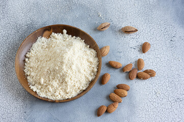 Almond flour in a wooden bowl, almonds on old light background