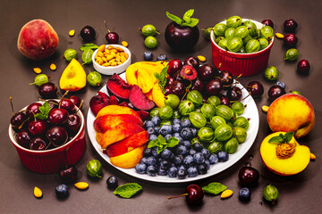 Assorted fresh berries of a cherry, gooseberry, blueberries, slices of ripe peach, plum and apricot, fragrant mint on a plate