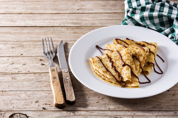 Sweet crepes with chocolate syrup on wooden table