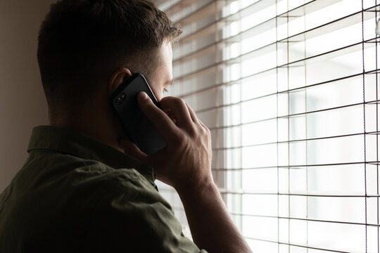 Closeup Photo From Back Of Man With Short Dark Hair Looking Through Window While Having Mobile Call On Black Cell Phone