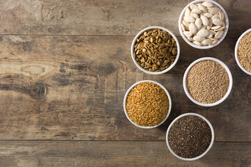 Assortment of different seeds in bowls on wooden table. Top view. Copy space