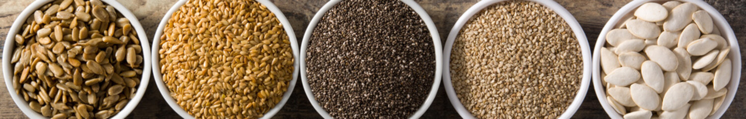 Assortment of different seeds in bowls on wooden table.  Panorama view. Top view