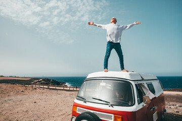 one man alone and isolated standing with opened arms on a minivan or camper having fun and smiling - digital nomad people lifestyle at the beach with freedomconcept with the sea at the background