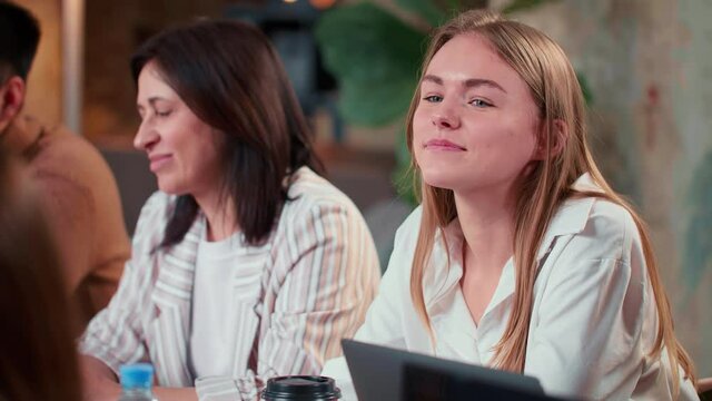 Happy excited 20s Caucasian manager business woman sits at creative team office meeting with middle aged colleague.