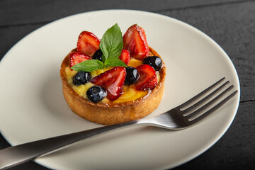 Fruit cake with berries, vanilla cream and mint leaves on white plate with a fork, close up view