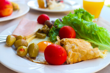 Continental breakfast served with fried egg, olives, cherry tomatoes, lettuce, orange juice, and a slice of bacon. Healthy food. Close-up, selective focus.