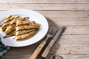 Sweet crepes with chocolate syrup on wooden table with copy space