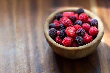 Red and black raspberries on a wooden plate. Ripe and fresh organic berries on a wooden background. Sunlight falls from the window. Blurred background.