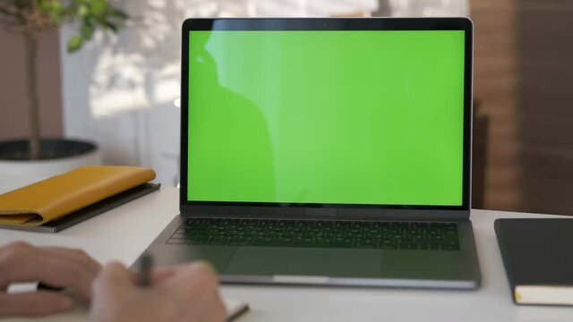 Young student looking at green screen laptop computer in living room watching movie, video content. Over shoulder close up view. Business woman or female freelancer working from home office. Close up