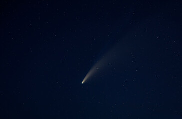 The bright comet Neowise flies overhead in the summer sky over the glow of a nearby town