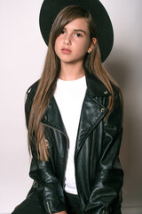 A teenage girl in a trendy leather jacket and an even hat on a white background. Teenage fashion. Street fashion. Beauty and fashion
