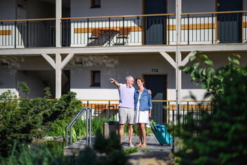 Senior couple with luggage outside apartment on holiday.