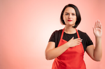 Woman employed at supermarket with red apron and black t-shirt showing oath